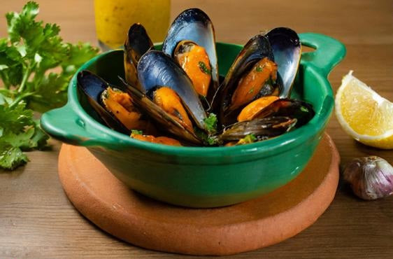 mejillones cocinados en cazuela verde sobre plato de barro