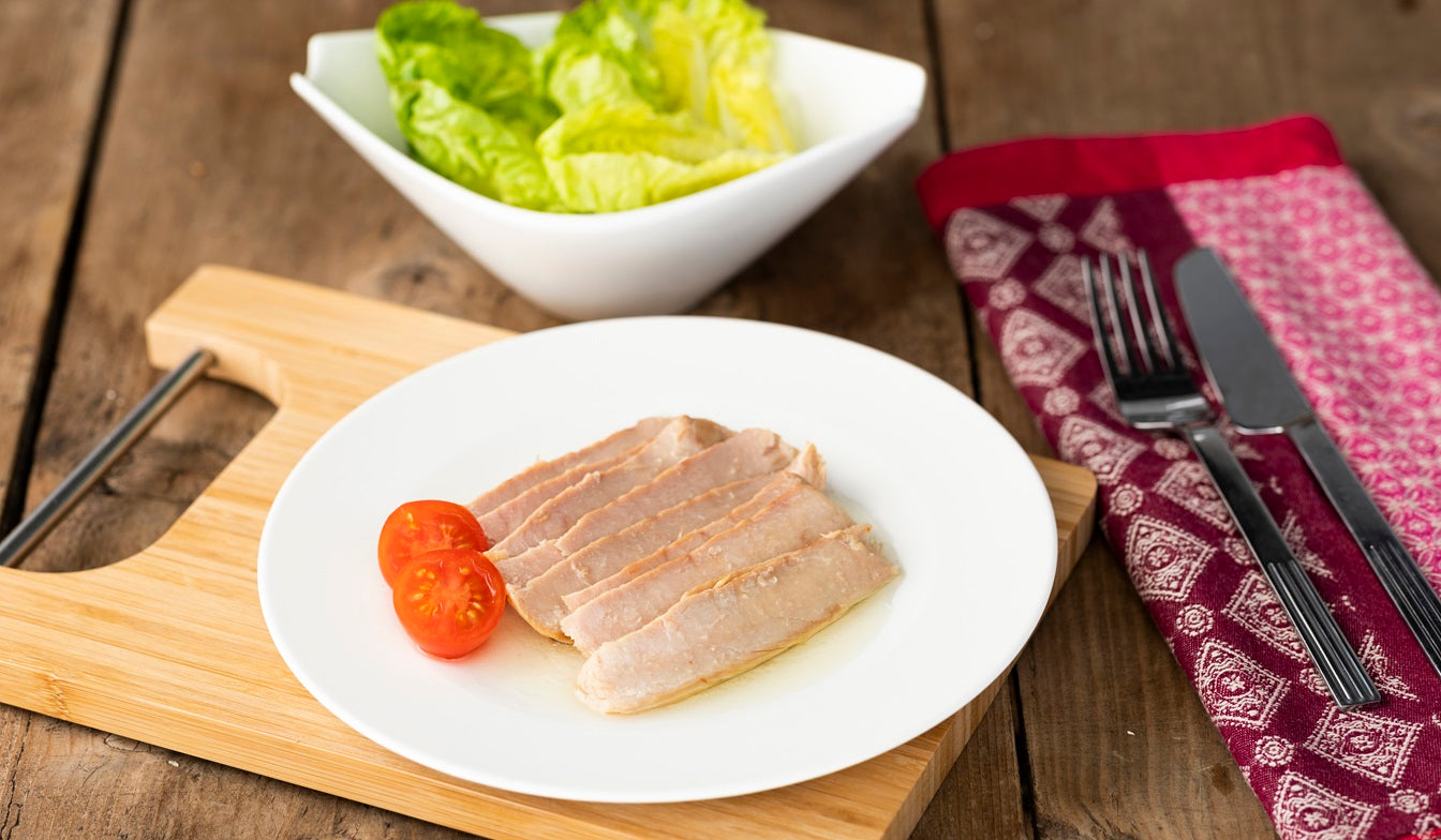 en una mesa de madera un bol de ensalada con un plato blacno de ventresca en aceite de oliva con tomate cherry